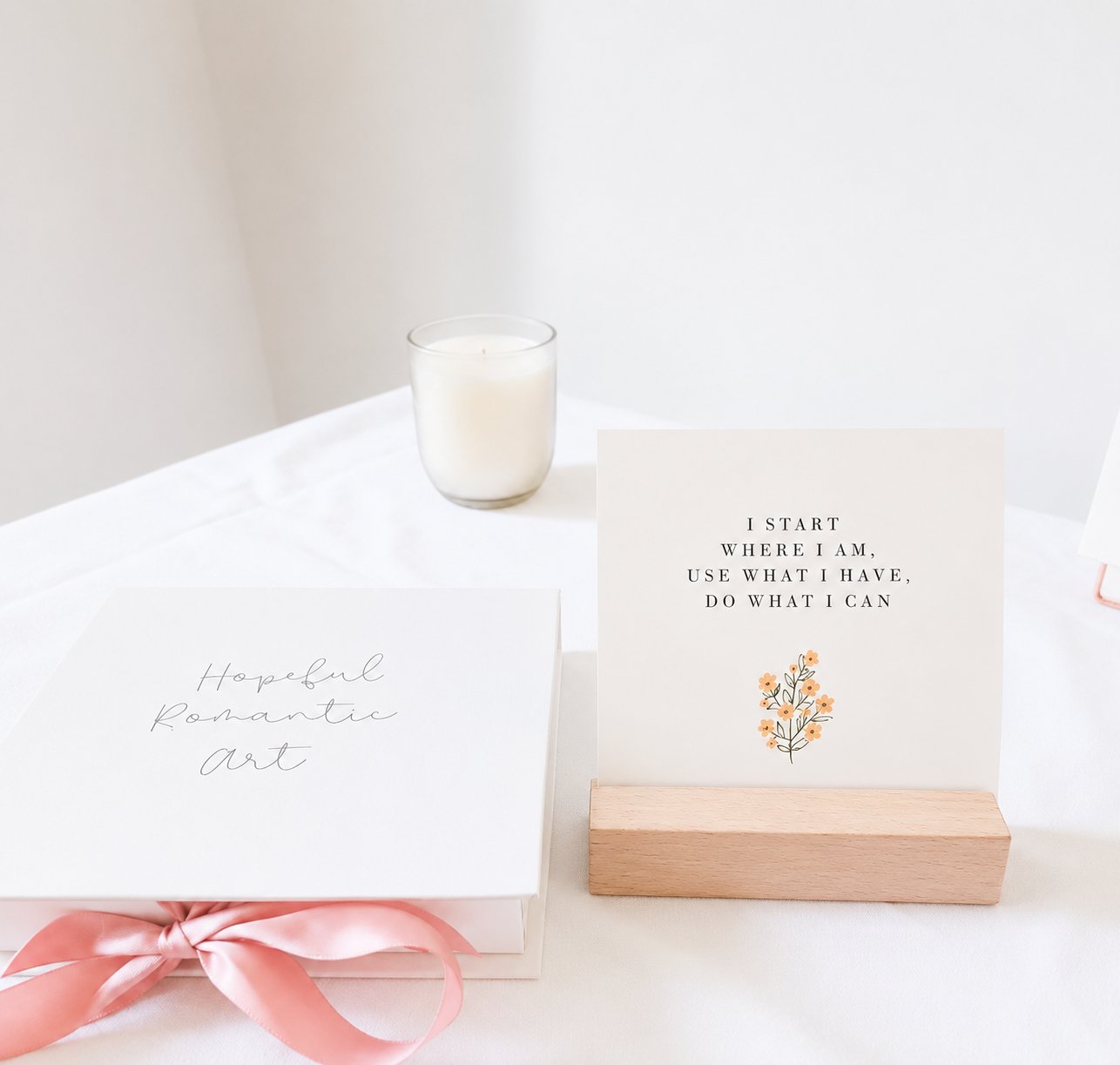 Affirmation card displayed in a wooden holder beside a Hopeful Romantic Art gift box with a pink ribbon and candle
