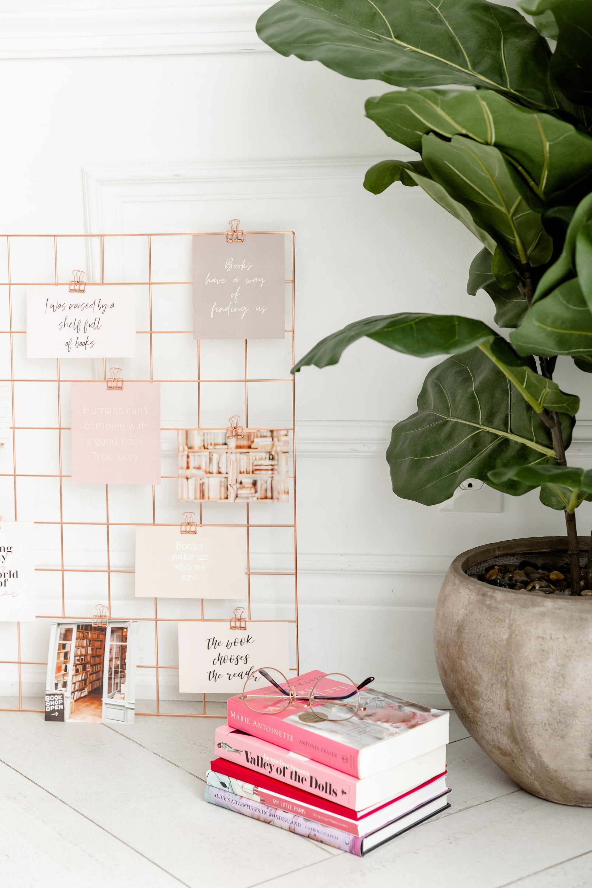 Bookish vision board cards styled on a wall grid beside stacked books and a plant