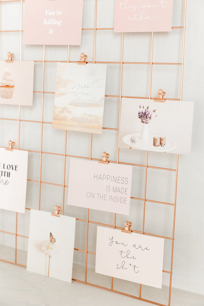 Rose gold bulldog clips used to display cards on a wall grid