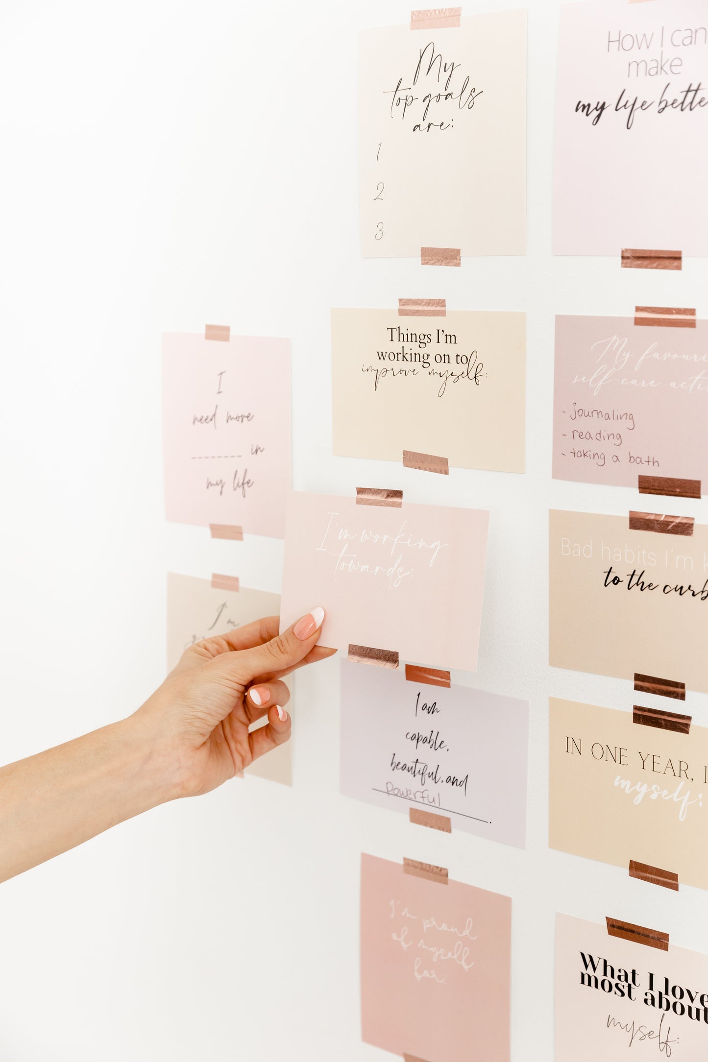 Goal-setting vision board cards displayed on a wall with a hand adding a pastel affirmation card.