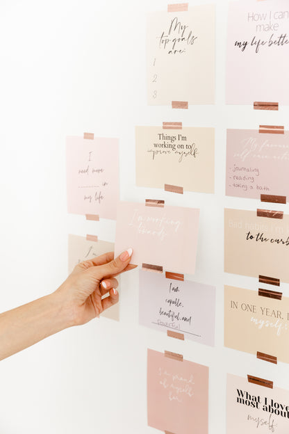 Goal-setting vision board cards displayed on a wall with a hand adding a pastel affirmation card.