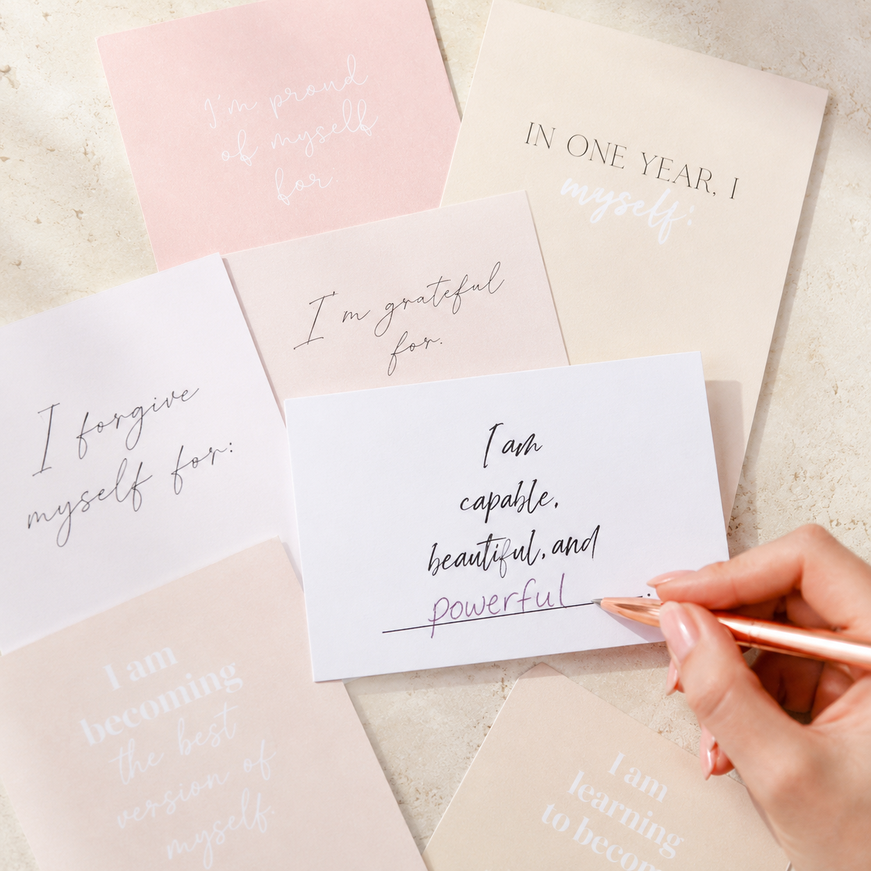 Goal-setting vision board cards with a handwritten affirmation card being filled in with a rose gold pen