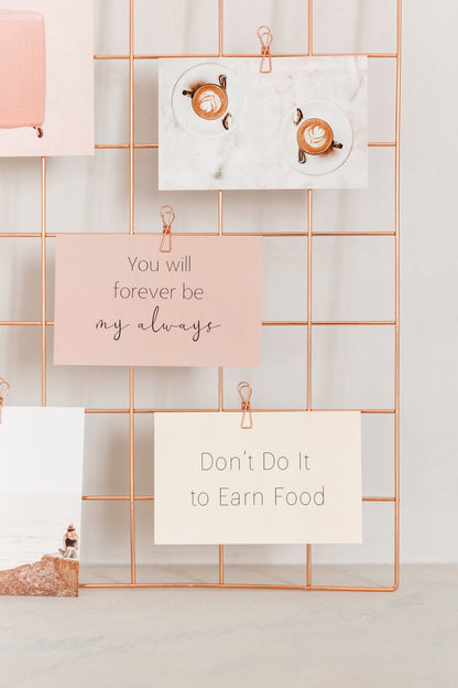 Motivational quote cards clipped to a rose gold grid for a vision board