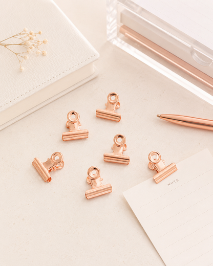 Rose gold bulldog clips styled on a neutral desk with stationery accessories