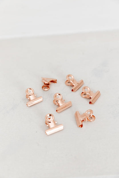 Set of 15 rose gold bulldog clips arranged on a white background