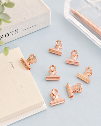 Rose gold bulldog clips styled with a planner, note cards, and pen