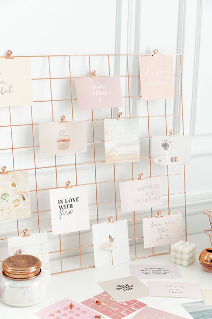 Rose gold bulldog clips styled on a wall grid with vision board cards and desk decor