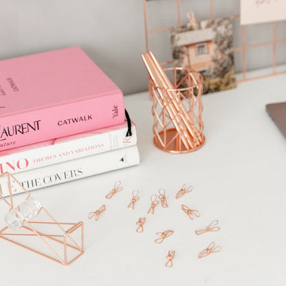 Rose gold wire clips scattered on white desk with fashion books and geometric accessories