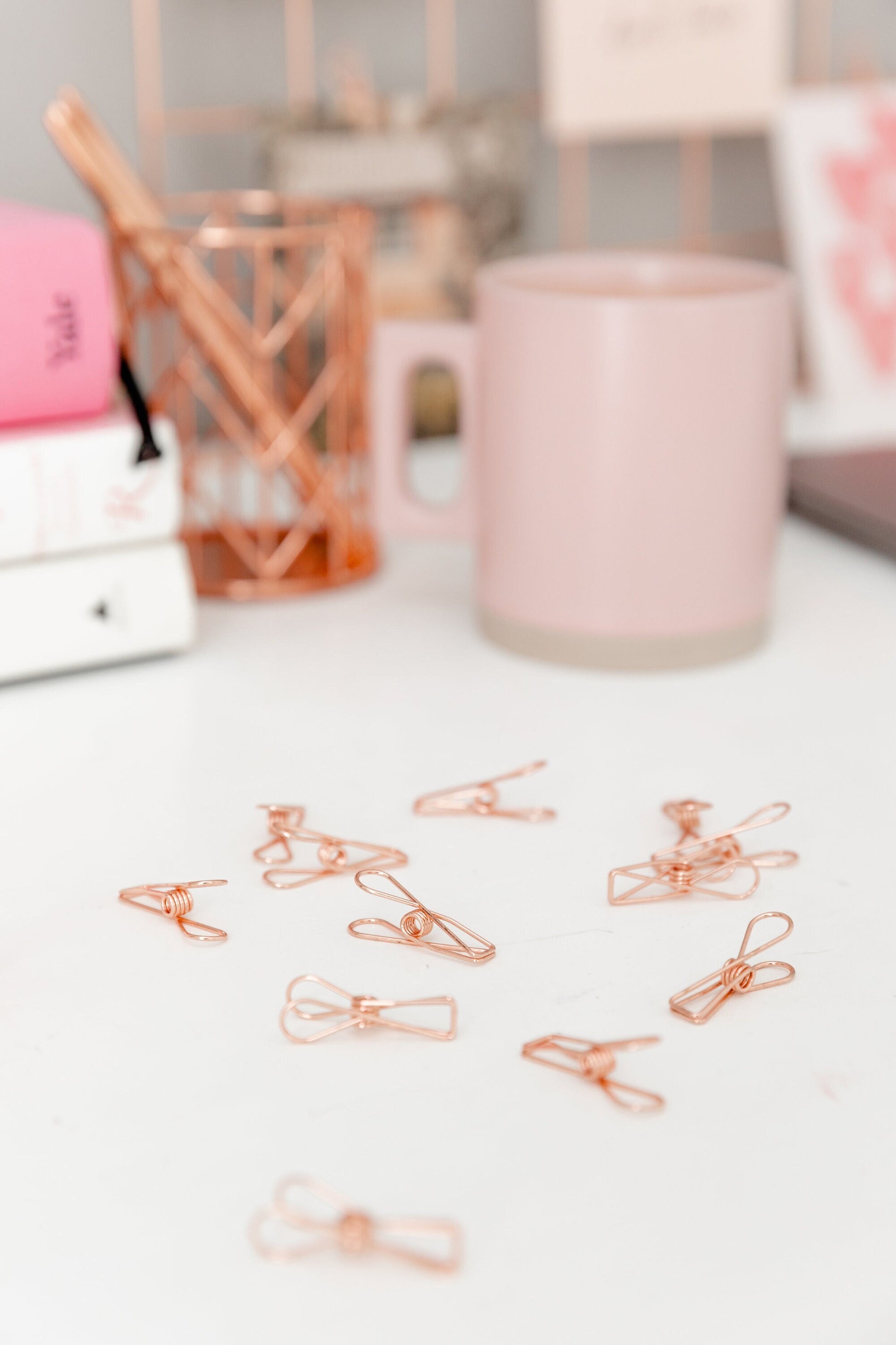 Rose gold wire clips on a desk with pink books and stationery