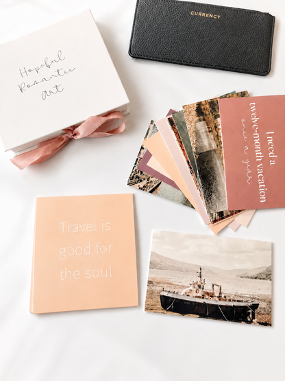 Travel vision board cards styled with a keepsake box, currency pouch, travel quote card, and boat image card on a bright white flat lay