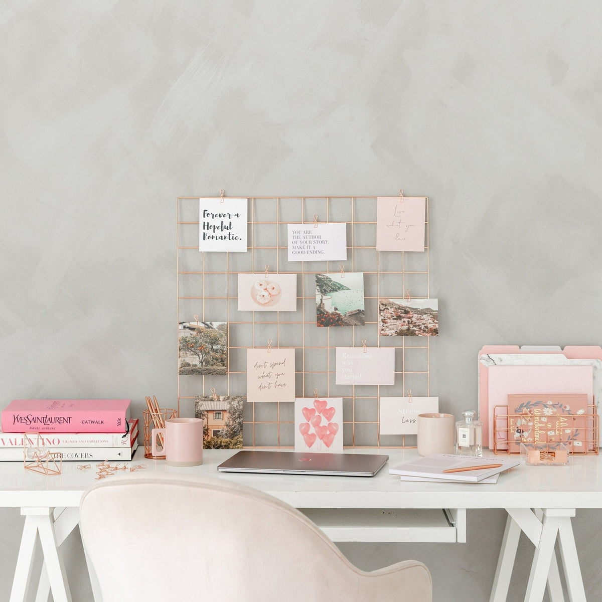 Rose gold vision board grid displayed above a desk with quote and image cards clipped to the grid